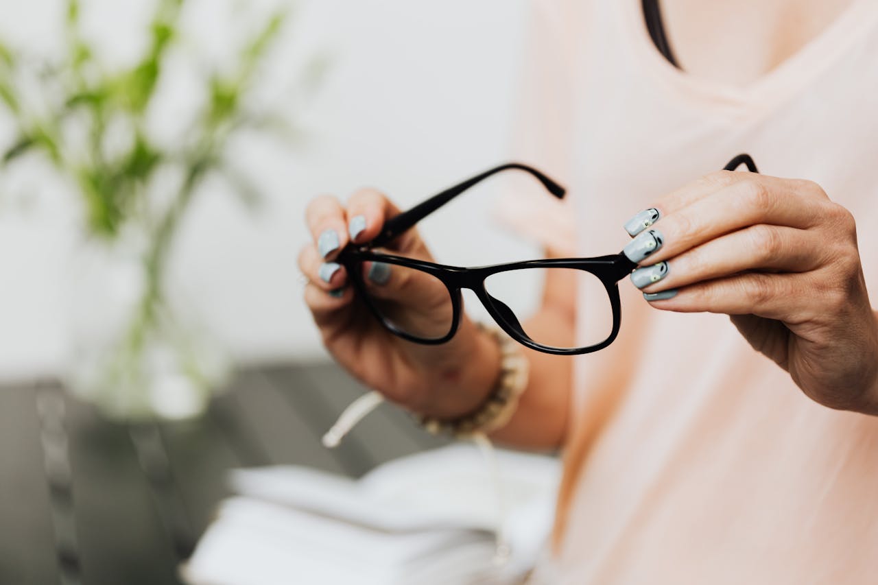 Close-up of a woman holding black eyeglasses with manicured nails indoors.