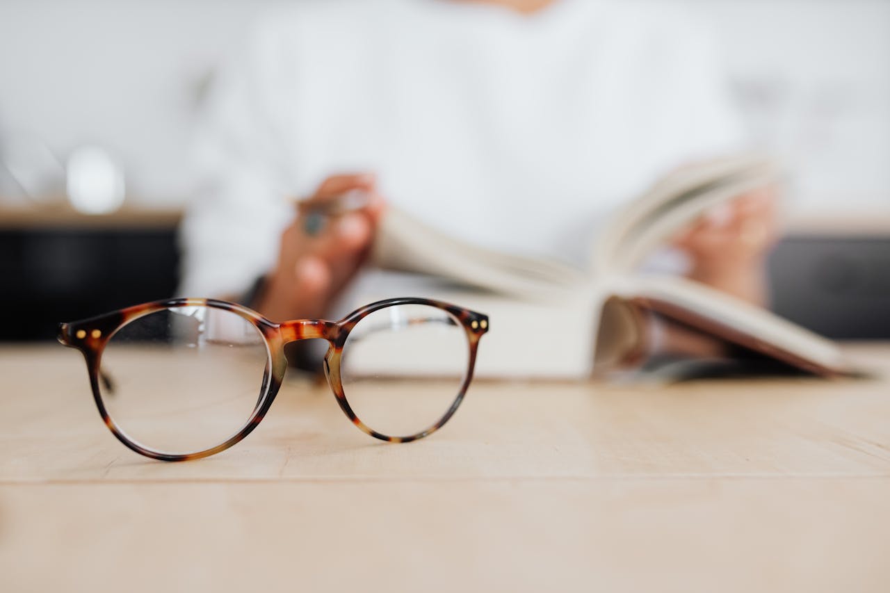 Tortoiseshell glasses on table with an open book, suggesting reading or study.
