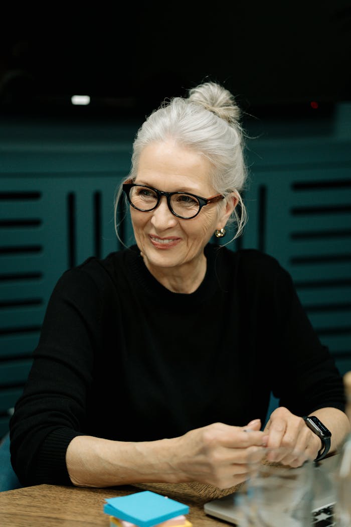 Elderly woman with gray hair wearing eyeglasses during a business meeting indoors.