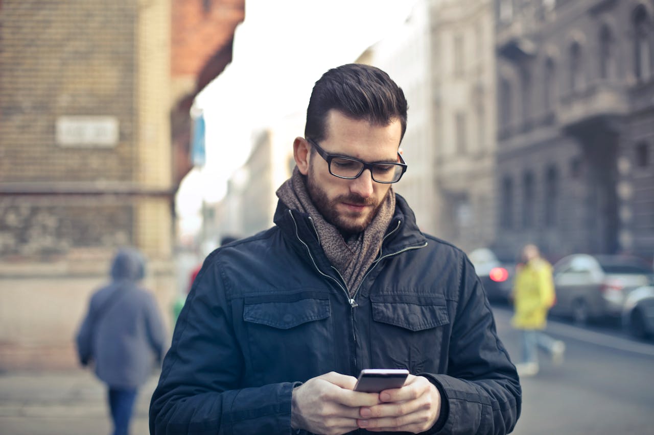 Home Adult man with glasses using a smartphone on a city street in Budapest, Hungary.