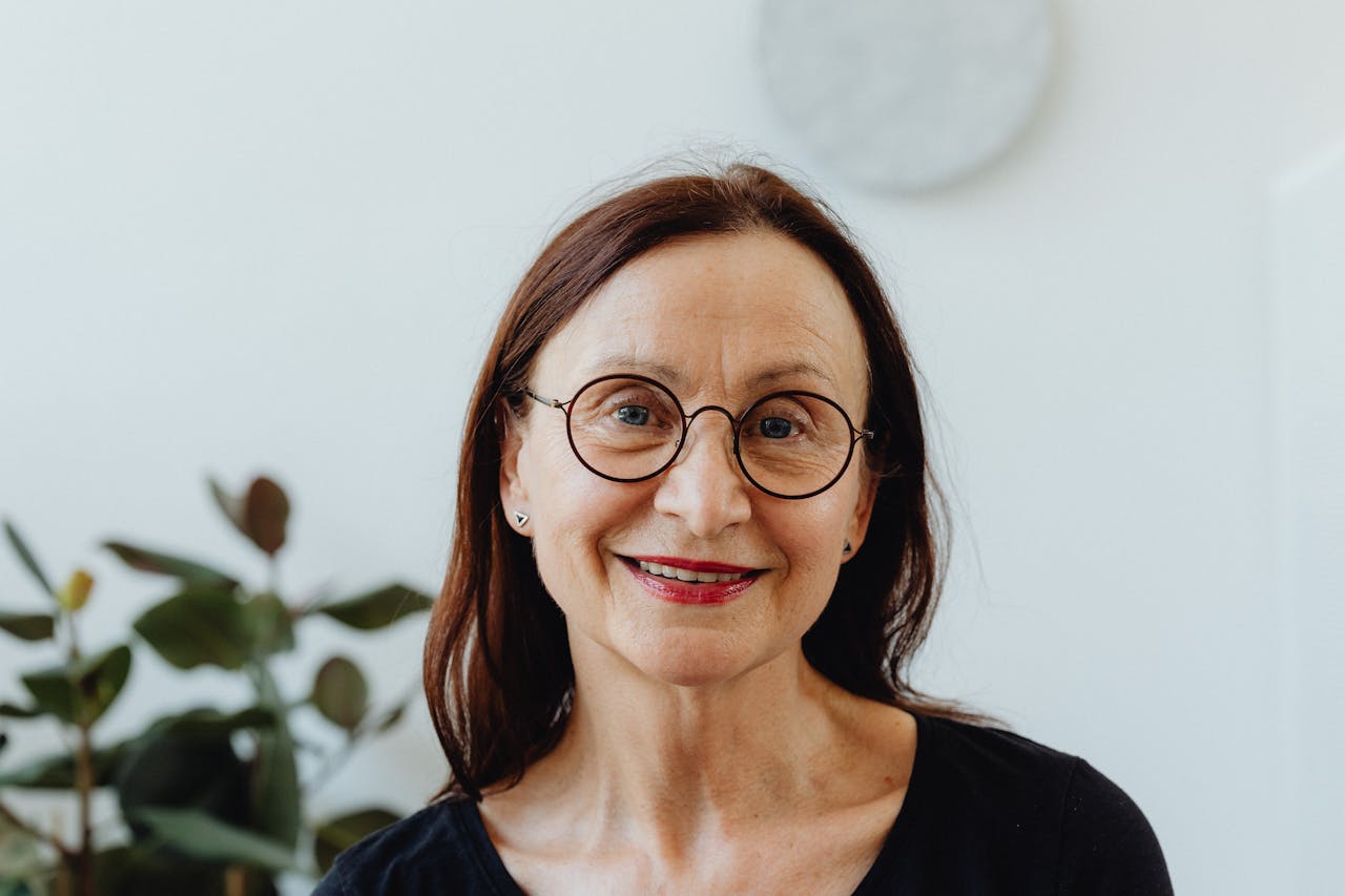 Home Portrait of a smiling senior woman wearing glasses against a bright indoor background.